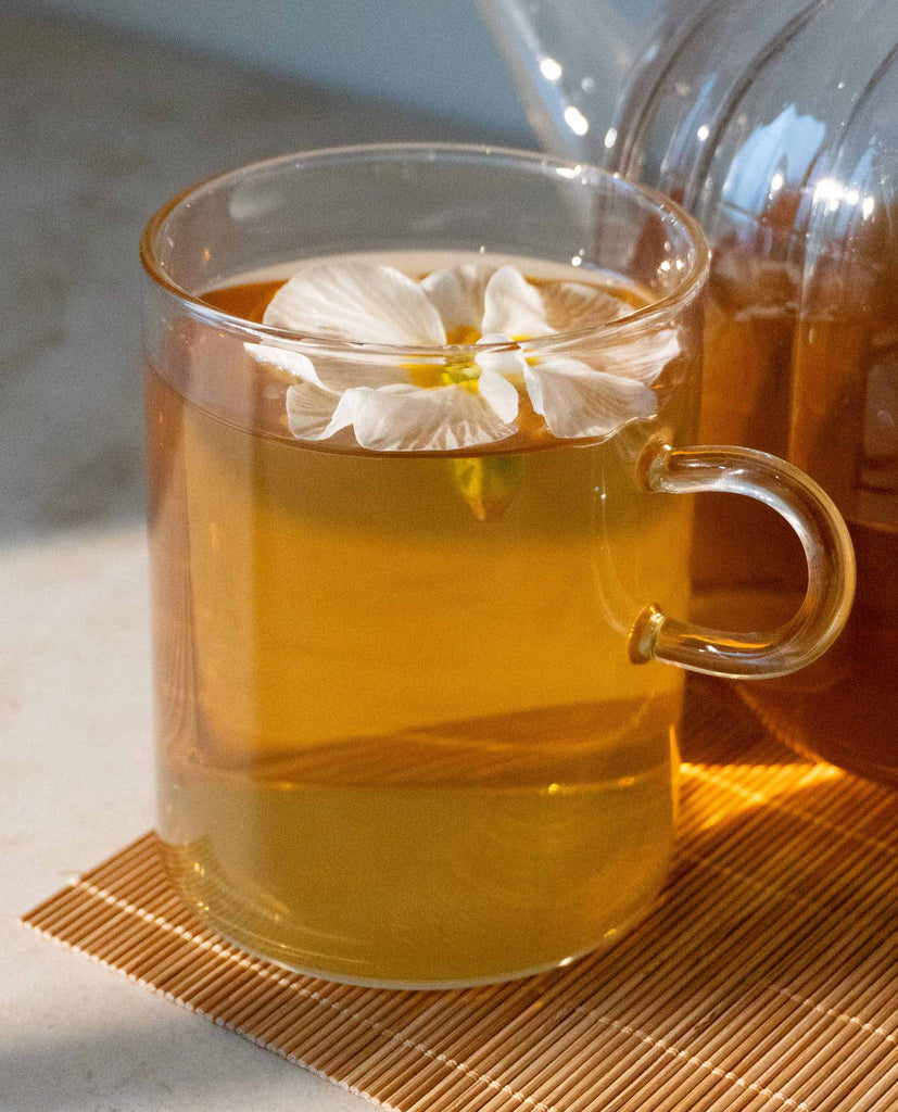Blooming Bliss calming herbal tea steeped in glass – 100% organic blend for focus and feminine balance. Pure plant-based tea for mental clarity and energy reset.