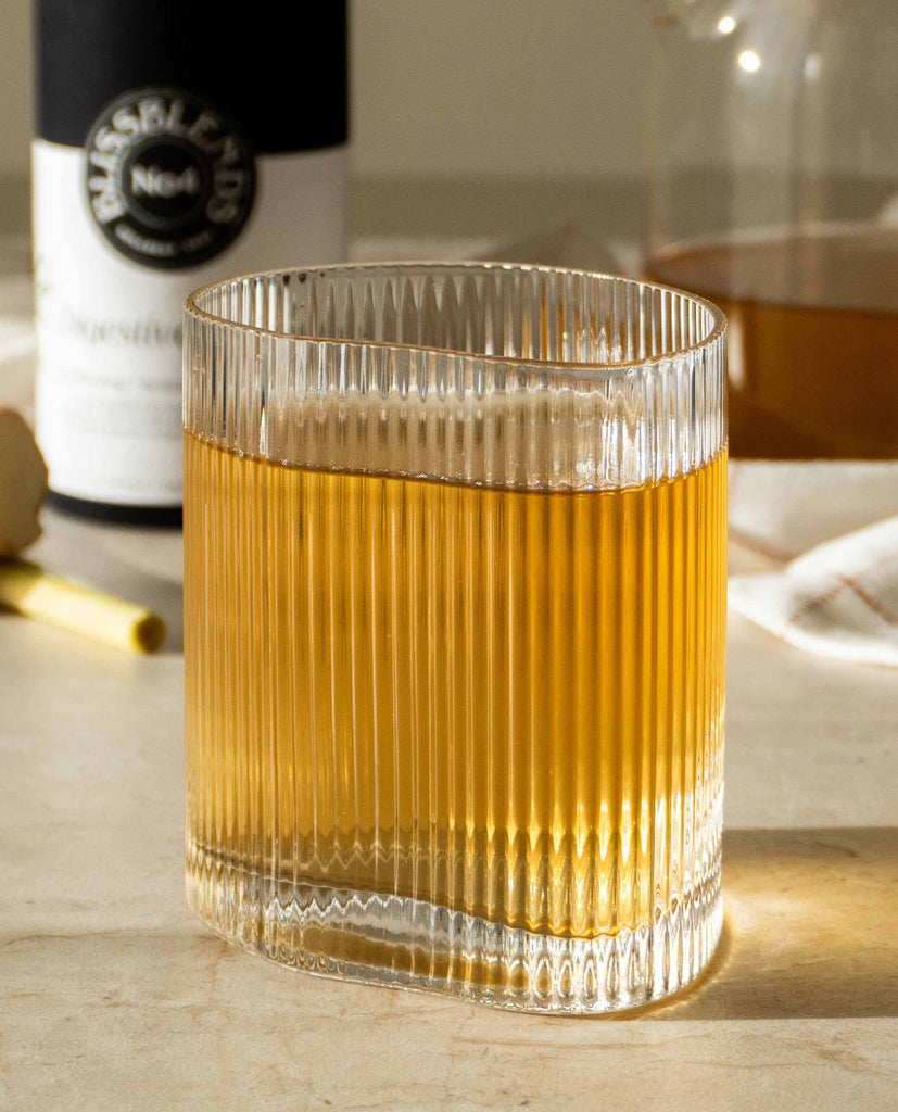 Golden herbal tea from BlissBlends Digestive Brew shown in a ribbed glass. Anti-bloating morning tea ritual for digestion and gut wellness.